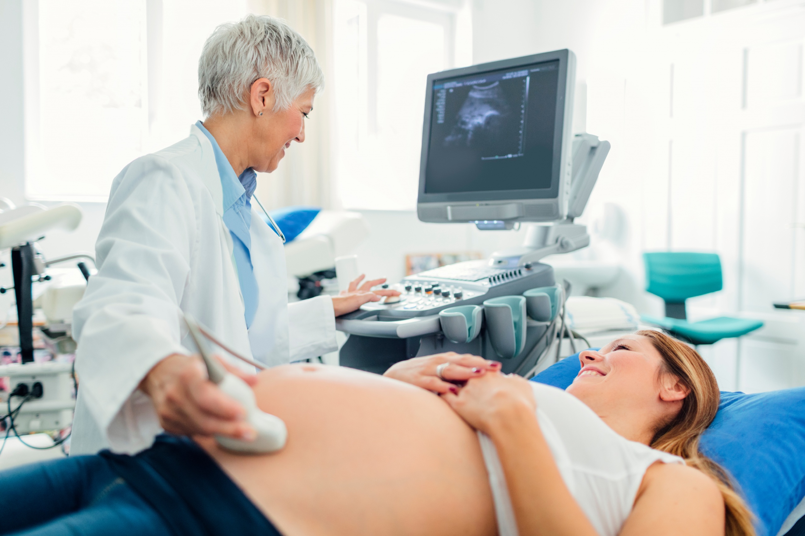 Pregnant woman and her male doctor in a consultation. Woman lying down while her doctor doing ultrasound examination. Young woman looking at her doctor.